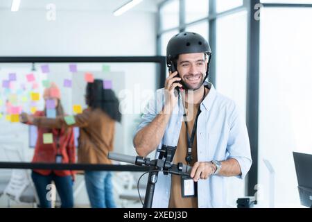 Portrait of smiling businessman talking on mobile phone while colleague using scooter in office Stock Photo