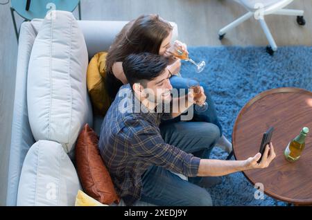 Happy couple drinking wine and using smartphone at home in the living room Stock Photo