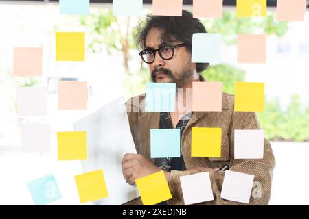 A creative professional brainstorming new ideas by writing them on sticky notes. A businessman brainstorming ideas by writing them on sticky notes and Stock Photo