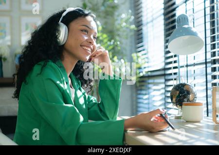 Young woman with headphones listening to music while sitting at table in room Stock Photo