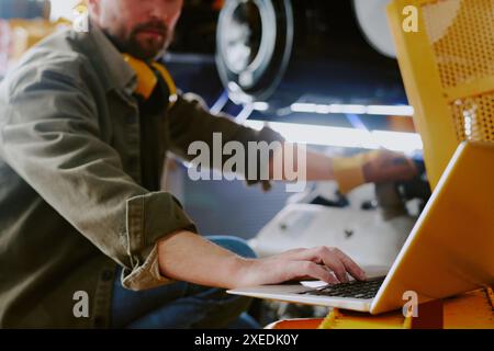 Selective focus shot of bearded repairman using laptop while fixing parts of industrial machine at work Stock Photo