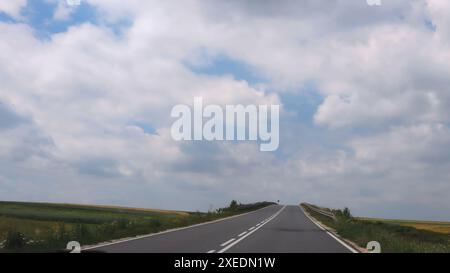 A road in the middle of a field against a sky of clouds Stock Photo