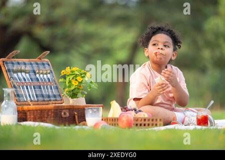 Happy family enjoying a picnic in the park, with kid eating jam bread, surrounded by nature Stock Photo