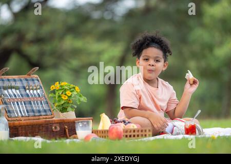 Happy family enjoying a picnic in the park, with kid eating jam bread, surrounded by nature Stock Photo