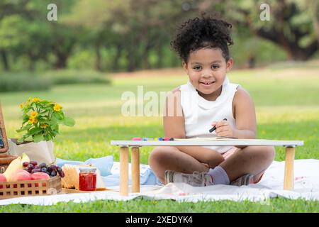 Happy family enjoying a picnic in the park, Girl are having fun drawing on paper placed on the table. Stock Photo