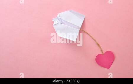 Concept of love for traveling by plane with paper airplane pulling a heart shaped paper cutout tied by a jute rope on pink background. Stock Photo