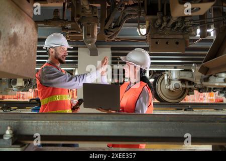 Male and female engineers work together in an electric repair station. Inspecting the undercarriage of electric train that are b Stock Photo