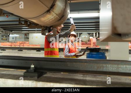 Male and female engineers work together in an electric repair station. Inspecting the undercarriage of electric train that are b Stock Photo
