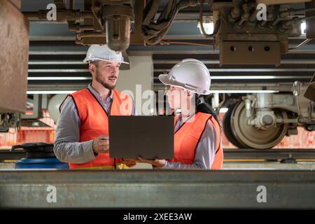 Male and female engineers work together in an electric repair station. Inspecting the undercarriage of electric train that are b Stock Photo