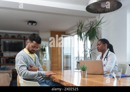 Young man visiting woman doctor in doctors office, having health issues with pain, talking with general practitioner in white coat with stethoscope at Stock Photo