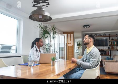 Young man visiting woman doctor in doctors office, having health issues with pain, talking with general practitioner in white coat with stethoscope at Stock Photo