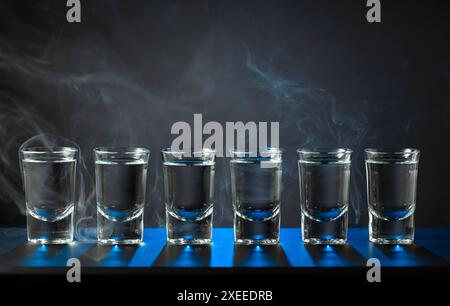 Alcoholic shots of vodka or strong drink in small glasses on a black background. Blue backlight. Copy space. Stock Photo