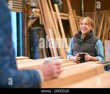 Male And Female Carpenter Working In Woodwork Workshop Talking On Coffee Break Stock Photo