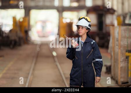 Portrait of railway technician worker in safety vest and helmet working and using a walkie talkie at train repair station Stock Photo