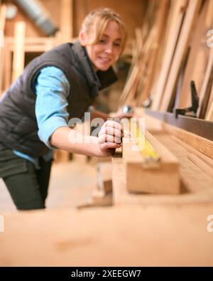Female Carpenter Working In Woodwork Workshop Measuring Wood For Project Stock Photo