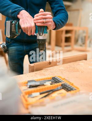 Close Up Of Carpenter At Workbench In Workshop Using Cordless Electric Drill Stock Photo