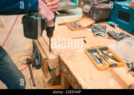 Close Up Of Carpenter At Workbench In Workshop Using Cordless Electric Drill Stock Photo