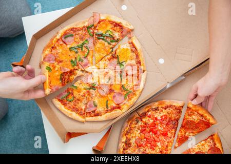 Two people are taking slices of pizza from open delivery boxes Stock Photo