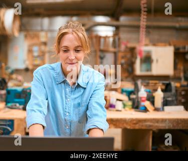Female Carpenter Working In Woodwork Workshop Using Laptop Stock Photo