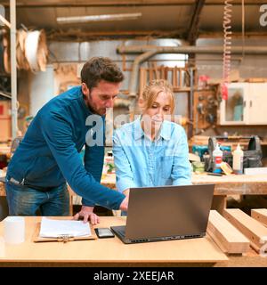 Male And Female Carpenters Working In Woodwork Workshop Using Laptop Together Stock Photo