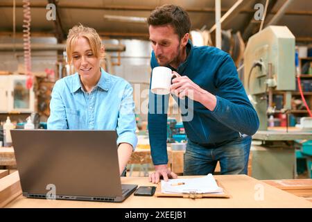 Male And Female Carpenters Working In Woodwork Workshop Using Laptop Together Stock Photo