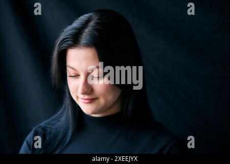 Studio Shot Of Young Woman With Thoughtful Expression Against Black Background Stock Photo