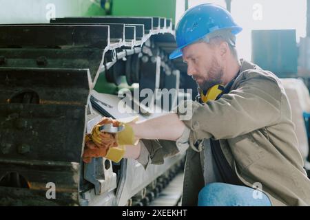 Medium shot of Caucasian male mechanic using wrench while repairing bulldozer undercarriage, copy space Stock Photo