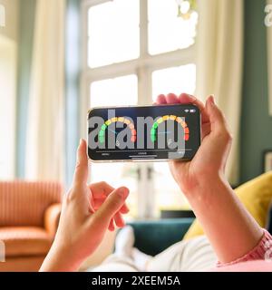 Close Up Of Woman Looking At Screen Of Energy Smart Meter On Mobile Phone Relaxing On Sofa At Home Stock Photo