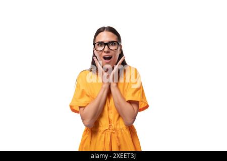 Young pretty brunette lady dressed in a yellow dress looks at the camera in surprise Stock Photo