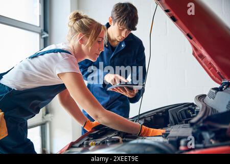 Female Car Auto Mechanic With Trainee Looking Under Bonnet Of Car Using Digital Tablet Stock Photo