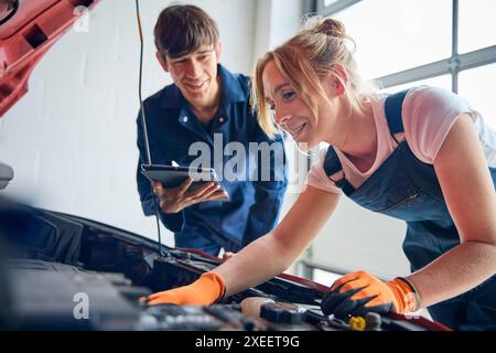 Female Car Auto Mechanic With Trainee Looking Under Bonnet Of Car Using Digital Tablet Stock Photo