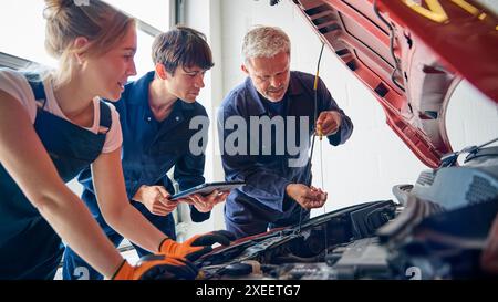 Team Of Car Auto Mechanics With Trainees Looking Under Bonnet Of Car Using Digital Tablet Stock Photo