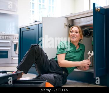 Female Plumber Fixing Waste Disposal Unit In Domestic Kitchen Sink Stock Photo