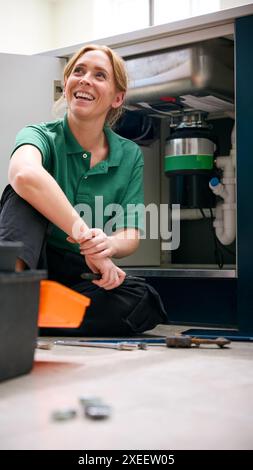Female Plumber Fixing Waste Disposal Unit In Domestic Kitchen Sink Stock Photo