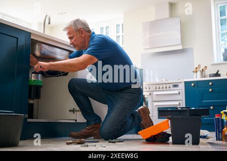 Mature Male Plumber Fixing Waste Disposal Unit In Domestic Kitchen Sink Stock Photo