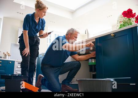 Male Plumber With Female Trainee Using Digital Tablet Fixing Waste Disposal Unit In Kitchen Sink Stock Photo