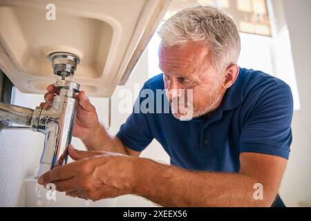 Close Up Of Mature Male Plumber Fixing Leak In Domestic Bathroom Sink Or Basin Stock Photo