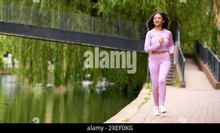 Woman Wearing Fitness Clothing Running Along Path By River In Urban Area Stock Photo