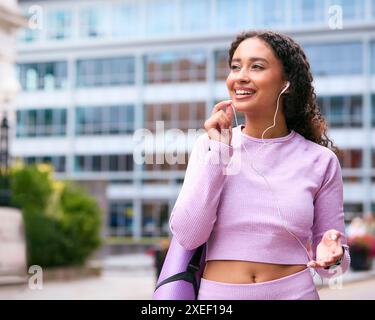 Woman Wearing Fitness Clothing Outdoors Taking Phone Call On Earphone Mic Connected To Mobile Phone Stock Photo
