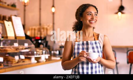 Confident Young Woman Wearing Apron Working In Coffee Shop Or Cafe Stock Photo