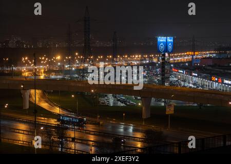 On night roads, cars drive over a bridge and a road junction. Urban cityscape Stock Photo