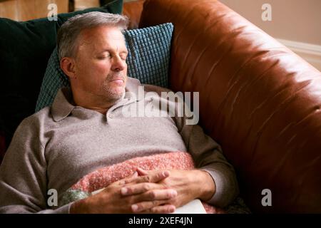 Mature Man At Home In Winter Jumper Sleeping On Sofa With Warm Blanket Stock Photo