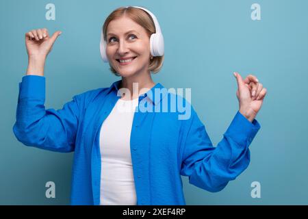 Middle age business concept. 50s woman with headphones without wire dancing on blue background copy space Stock Photo
