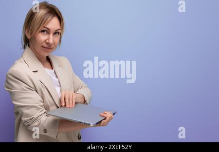 Successful blond young woman in a business jacket with a laptop on a studio background Stock Photo