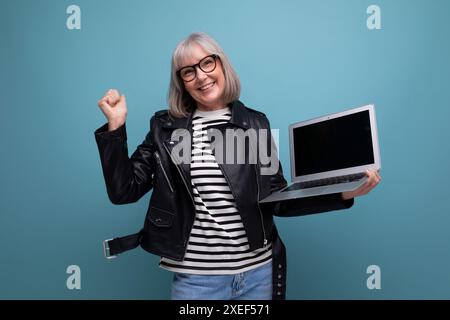 Joyful modern 50s mature old lady freelancer with gray hair surfs the internet using laptop with mockup on bright background Stock Photo