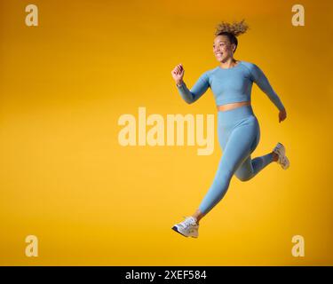 Studio Shot Of Woman Wearing Gym Fitness Clothing In Mid-Air Exercising On Yellow Background Stock Photo