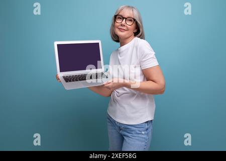 Middle age business. middle aged woman with gray hair re-learn remote profession using laptop on studio background with copy spa Stock Photo