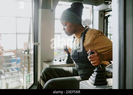 Medium shot of young African American female quality control specialist sitting in new bulldozer cabin doing test drive Stock Photo