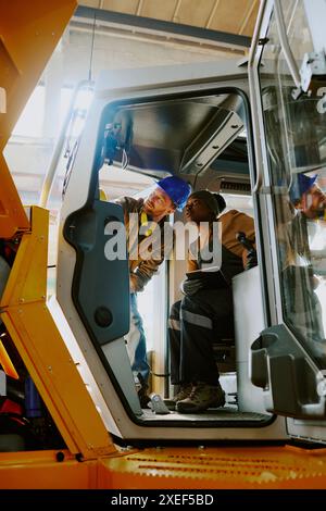 Vertical shot of two ethnically diverse engineers doing quality control of new bulldozer at work in modern factory Stock Photo