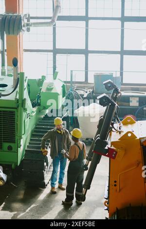 High angle view shot of two ethnically diverse male and female engineers having conversation at work in dozer production factory Stock Photo